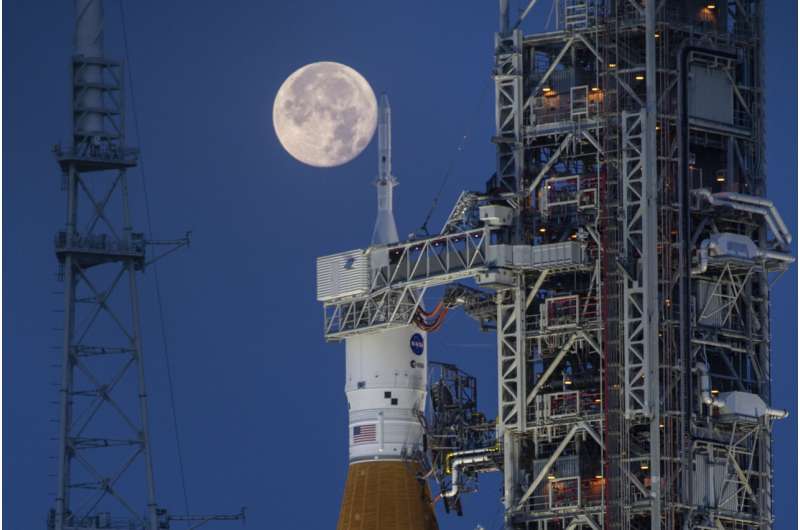 Полная луна видна за системой космического запуска «Артемида I» (SLS), а космический корабль «Орион» на вершине мобильной ракеты-носителя готовится к генеральной репетиции для отработки сроков и процедур запуска на стартовом комплексе 39B в Космическом центре НАСА Кеннеди во Флориде. 14 июня 2022 года. Во вторник, 9 января 2024 года, НАСА заявило, что астронавтам придется подождать до 2025 года, прежде чем полететь на Луну, и еще несколько лет, прежде чем приземлиться на нее. Фото: Кори Хьюстон/НАСА, AP. Новые задержки с запуском астронавтов НАСА на Луну, с высадкой экипажа до 2026 года